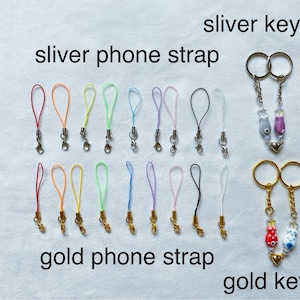 May include: Assortment of colorful phone straps and keychains.  The phone straps are made of thin cord and have silver or gold clasps. The keychains feature small, colorful glass charms.  The text "sliver keyring", "sliver phone strap", "gold phone strap", and "gold keyring" is visible in the image.