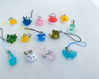 May include: A collection of 13 colorful, small, plastic charms with different sea creature designs. Each charm is attached to a string with a metal ring. The charms include a blue shark, a pink octopus, a green seahorse, a yellow pufferfish, a blue jellyfish, a green turtle, a blue stingray, a pink whale, a green seahorse, a yellow pufferfish, a blue jellyfish, a green turtle, and a blue stingray.