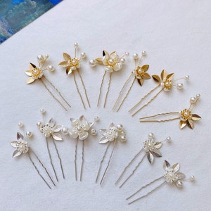 May include: A set of 10 gold and silver hair pins with pearl and leaf embellishments. The pins are arranged on a white surface.