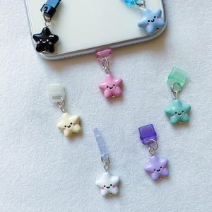 May include: A set of six colourful star-shaped phone charms with happy faces. Each charm is attached to a clear plastic phone holder.