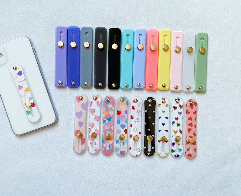 May include: Assortment of 18 phone grips with a variety of colors and patterns. The grips are made of silicone and have a small, round button on the back. The patterns include hearts, stripes, and polka dots.