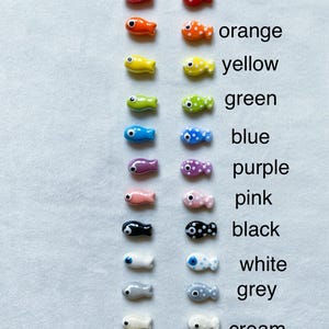 May include: Two rows of ceramic fish charms, one row with solid colors and the other with white spots. The colors are red, orange, yellow, green, blue, purple, pink, black, white, gray, and cream.