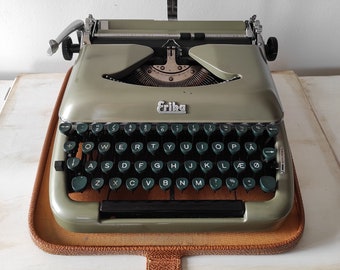 Op de afbeelding: Een groene vintage Erika typemachine met een bruine leren koffer. De typemachine heeft een standaard QWERTY-toetsenbord met groene toetsen en een zilveren retourtoets.