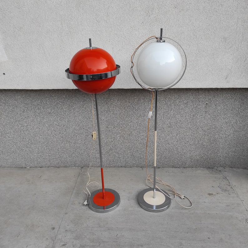 May include: Two modern floor lamps with chrome bases and round shades. One lamp has a red shade and the other has a white shade.