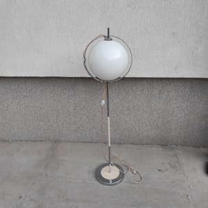 May include: A white globe lamp with a chrome stand and a white cord. The lamp is on a gray concrete floor.