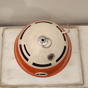 May include: A white and orange vintage lamp with a round, dome-shaped shade. The lamp has a cord and a switch on the side.