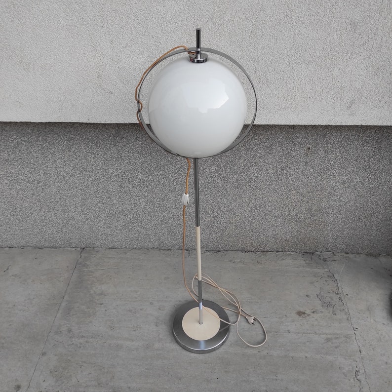 May include: A white globe lamp with a chrome frame and base. The lamp has a white cord and a white plug.