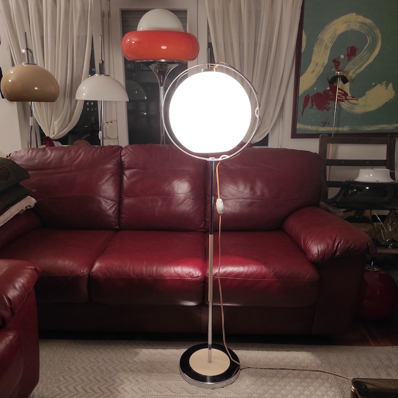 May include: A chrome floor lamp with a white globe shade and a red leather sofa in the background.
