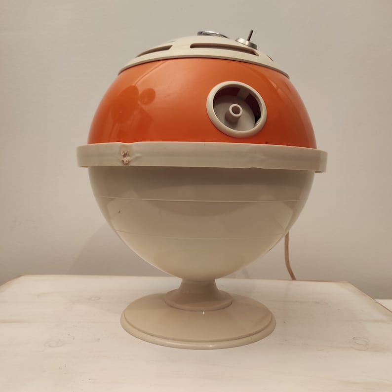 May include: A vintage orange and white ceramic electric heater shaped like a sphere with a round base. The heater has a cord and a small knob on the top.