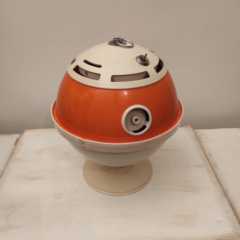 May include: A vintage orange and white plastic table lamp with a round base and a spherical shade. The shade has a series of holes and a small knob on top.
