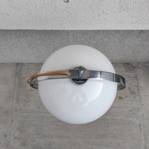 May include: A white globe lamp with a chrome ring and a brown leather strap. The lamp is on a gray surface.
