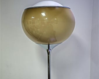 May include: A floor lamp featuring a spherical, amber-tinted glass shade with a white glass top section. The lamp is supported by a slender, polished chrome metal stem that connects to the base of the glass shade with a flared chrome collar.