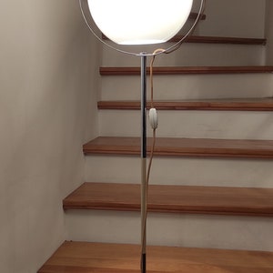 May include: A chrome floor lamp with a white globe shade and a circular chrome frame. The lamp is on a wooden floor with stairs in the background.