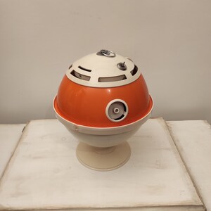 May include: A vintage orange and white plastic table lamp with a round base and a globe-shaped shade. The shade has a series of holes and a small metal ring on top.