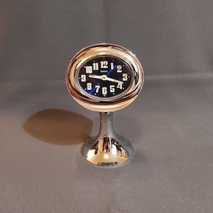 Puede incluir: Un reloj plateado con una esfera azul y números negros. El reloj está en un soporte y tiene la palabra "EUROPA" impresa en la esfera.