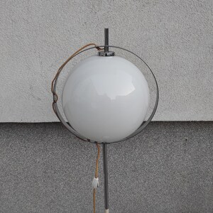 May include: A white globe lamp with a chrome frame and a brown cord. The lamp is on a white wall.