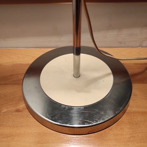 May include: A chrome floor lamp with a white circular base. The lamp has a single light bulb and a cord that plugs into an outlet.