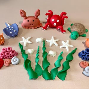 Könnte beinhalten: Eine Sammlung farbenfroher, handgefertigter Dekorationen zum Thema Meeresbewohner und Ozean. Enthält eine Krabbe, einen Oktopus, eine Schildkröte, einen Stechrochen, Seesterne, Korallen und Seetang.