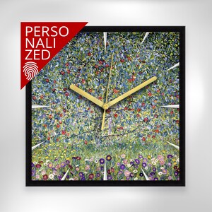 Puede incluir: Reloj de pared cuadrado con marco negro. La esfera del reloj presenta una pintura colorida de un árbol con manzanas rojas y un campo de flores. Las manecillas del reloj son doradas. La palabra "PERSONALIZED" está en rojo en la esquina superior izquierda.