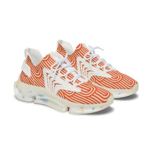 May include: A pair of athletic shoes with a white and orange wavy pattern. The shoes have white laces and accents, and a clear sole with colorful speckles. The design is modern and eye-catching.