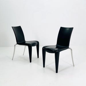 May include: Two black chairs with curved backs and sleek, modern design. The chairs have black seats and backs, with silver metal legs. The chairs are set against a white background.