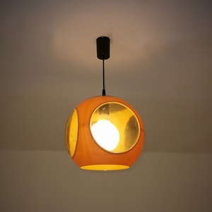 May include: A round, orange pendant light with three circular cutouts. The light is on and illuminates the room.