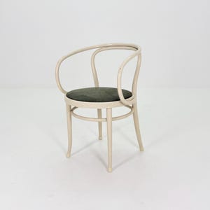 May include: A cream-colored armchair with a rounded back and armrests. The seat cushion is a dark green. The chair has four legs and a circular support near the base. The design is simple and elegant.