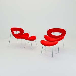 May include: Two sets of red, mid-century modern chairs and footstools. The chairs have an oval backrest with a cutout, and the footstools are kidney-shaped. All pieces have slender, silver metal legs.