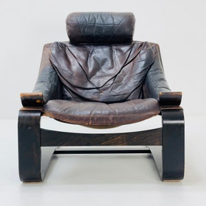 May include: A brown leather armchair with a high back and a wooden frame. The chair has a curved, modern design and is upholstered in a distressed leather.