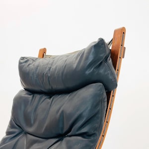 Puede incluir: Un sill&oacute;n de cuero azul oscuro con un marco de madera y un respaldo curvo. El sill&oacute;n tiene un asiento y un respaldo acolchados y c&oacute;modos.