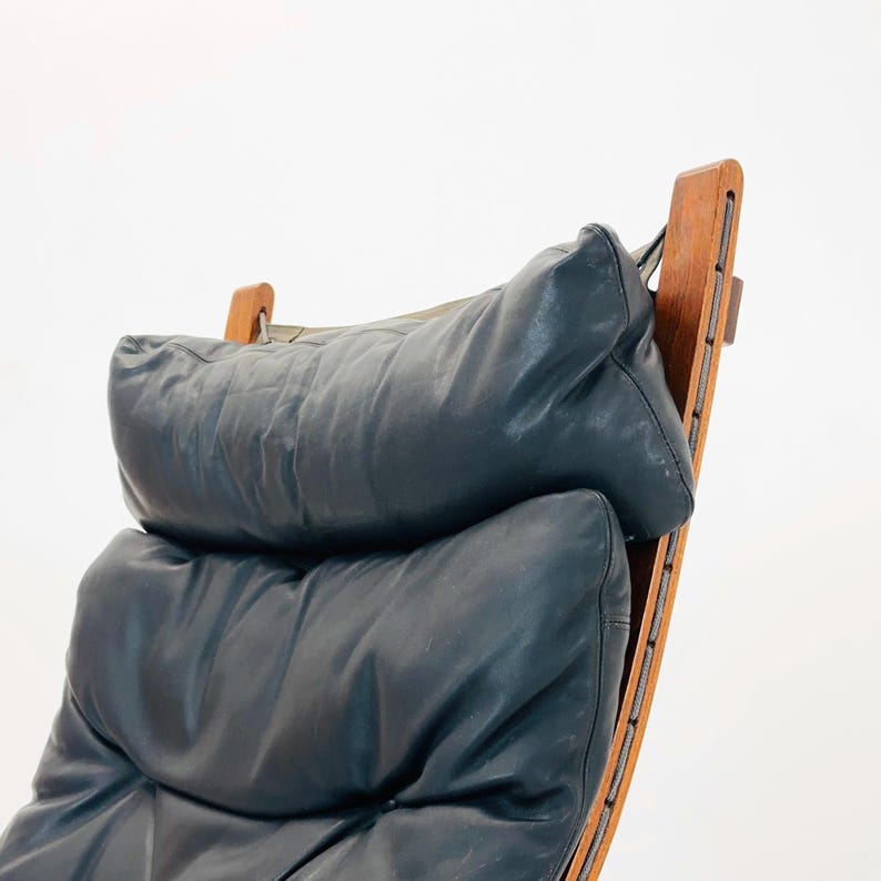 Puede incluir: Un sill&oacute;n de cuero azul oscuro con un marco de madera y un respaldo curvo. El sill&oacute;n tiene un asiento y un respaldo acolchados y c&oacute;modos.