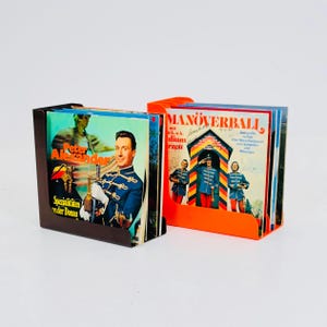 May include: Two vintage vinyl record holders, one brown and one orange, each filled with records. The brown holder features a record with Peter Alexander's image. The orange holder has a record with the title "Manöverball."