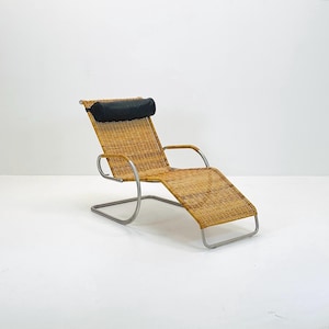 May include: A woven wicker chaise lounge with a black padded headrest. The lounge is made of metal and has a curved design.