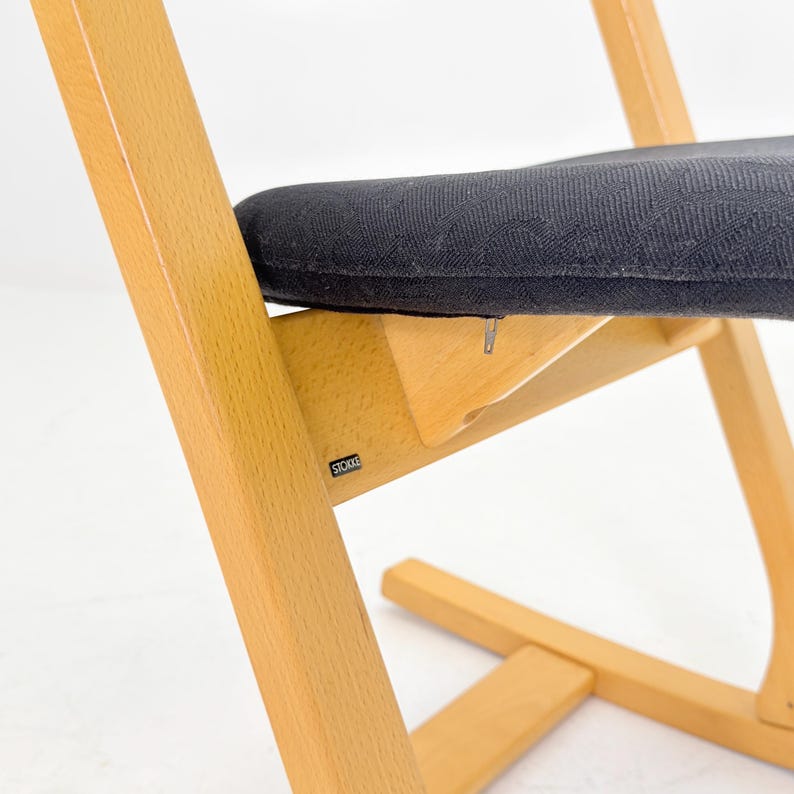 May include: A wooden high chair with a black patterned seat and backrest. The chair has a natural wood finish and a sturdy design. The chair is designed for children and has a footrest.