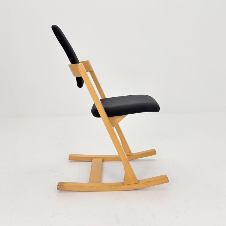 May include: A wooden rocking chair with a black seat and backrest. The chair has a curved base and a minimalist design. The frame is made of light-colored wood, and the seat and backrest are upholstered in black fabric.