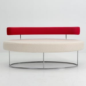 K&ouml;nnte beinhalten: Ein kreisf&ouml;rmiges Sofa mit einer cremefarbenen, strukturierten Sitzfl&auml;che und einer d&uuml;nnen, horizontalen roten R&uuml;ckenlehne. Das M&ouml;belst&uuml;ck wird von einem schlanken, ovalen Chrommetallrahmen getragen, der die Basis mit der R&uuml;ckenlehnenst&uuml;tze verbindet.