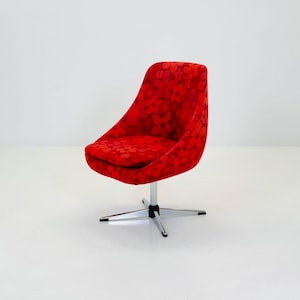 Könnte beinhalten: Ein roter Drehstuhl mit floralem Muster. Der Stuhl hat eine geschwungene Rückenlehne und Sitzfläche sowie ein chromfarbenes, sternförmiges Gestell. Der Stuhl steht vor einem weißen Hintergrund.