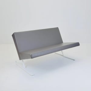 Könnte beinhalten: Ein moderner grauer Zweisitzer mit minimalistischem Design. Sitzfläche und Rückenlehne sind mit einem einfarbigen grauen Material bezogen. Der Rahmen besteht aus weißem Metall mit abgewinkelten Beinen zur Unterstützung. Der Zweisitzer ist für zwei Personen konzipiert.