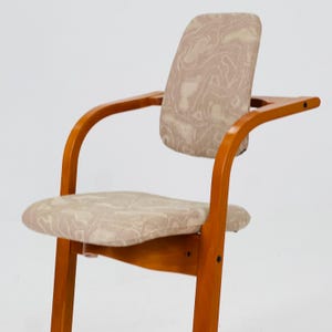 Pode incluir: Poltrona de madeira com acabamento castanho claro. O assento e o encosto s&atilde;o estofados em tecido bege com um padr&atilde;o subtil em espiral. A cadeira tem apoios de bra&ccedil;os curvos e um design simples e elegante, adequado para v&aacute;rios estilos de interiores.