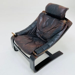 May include: A brown leather armchair with a curved wooden frame and a headrest. The chair has a worn, vintage look.