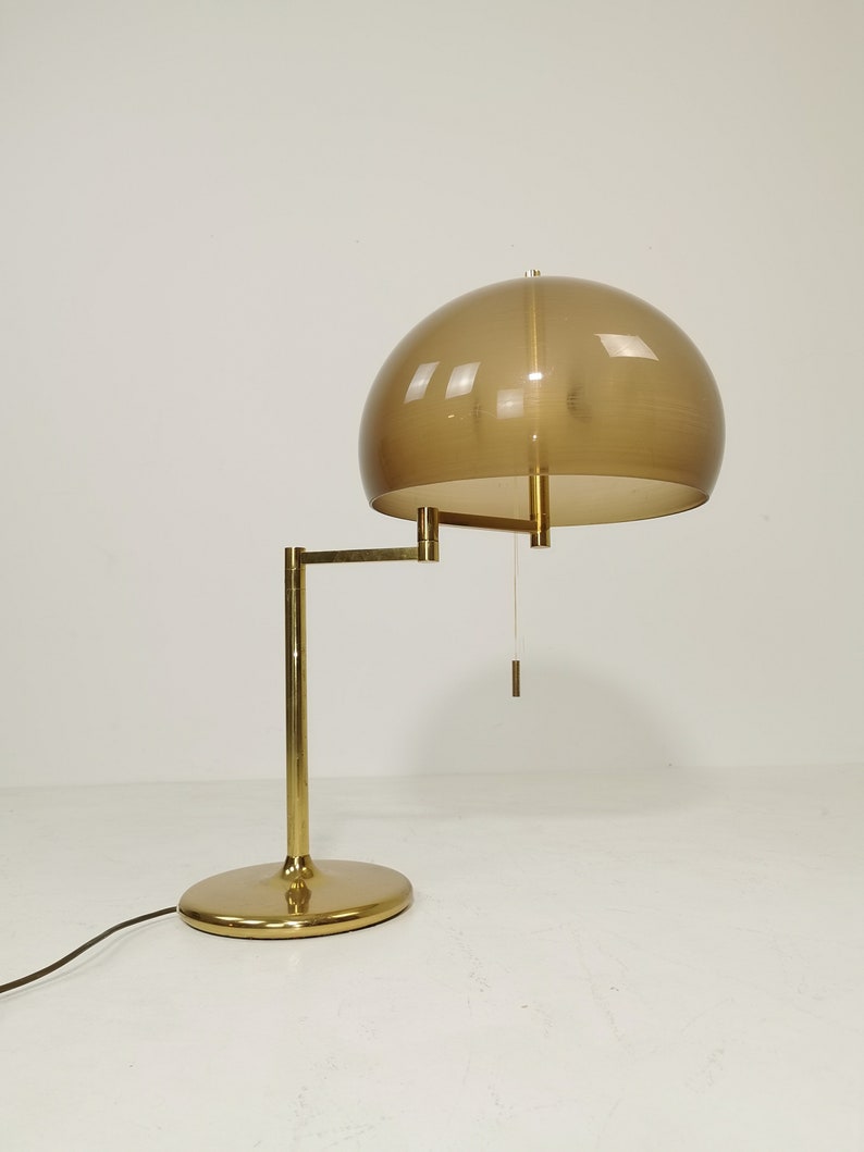 May include: A brass desk lamp with a brown glass shade. The lamp has a flexible arm and a round base.