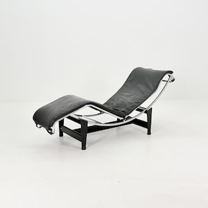 May include: A black leather chaise lounge with a chrome frame and black wooden supports. The chair has a curved design and is set against a white background. The headrest is slightly elevated.
