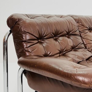 May include: A brown leather sofa with a tufted back and chrome legs. The sofa has a deep, comfortable seat and a relaxed, modern style.