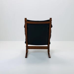 Puede incluir: Una silla de cuero negro con un marco de madera. La silla tiene un respaldo curvo y un dise&ntilde;o simple.