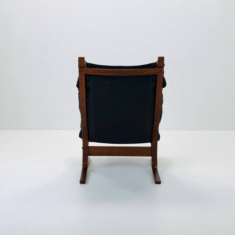 Puede incluir: Una silla de cuero negro con un marco de madera. La silla tiene un respaldo curvo y un dise&ntilde;o simple.