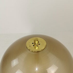 May include: A brown glass globe lampshade with a brass top and a small brass knob. The lampshade has a smooth, shiny finish.