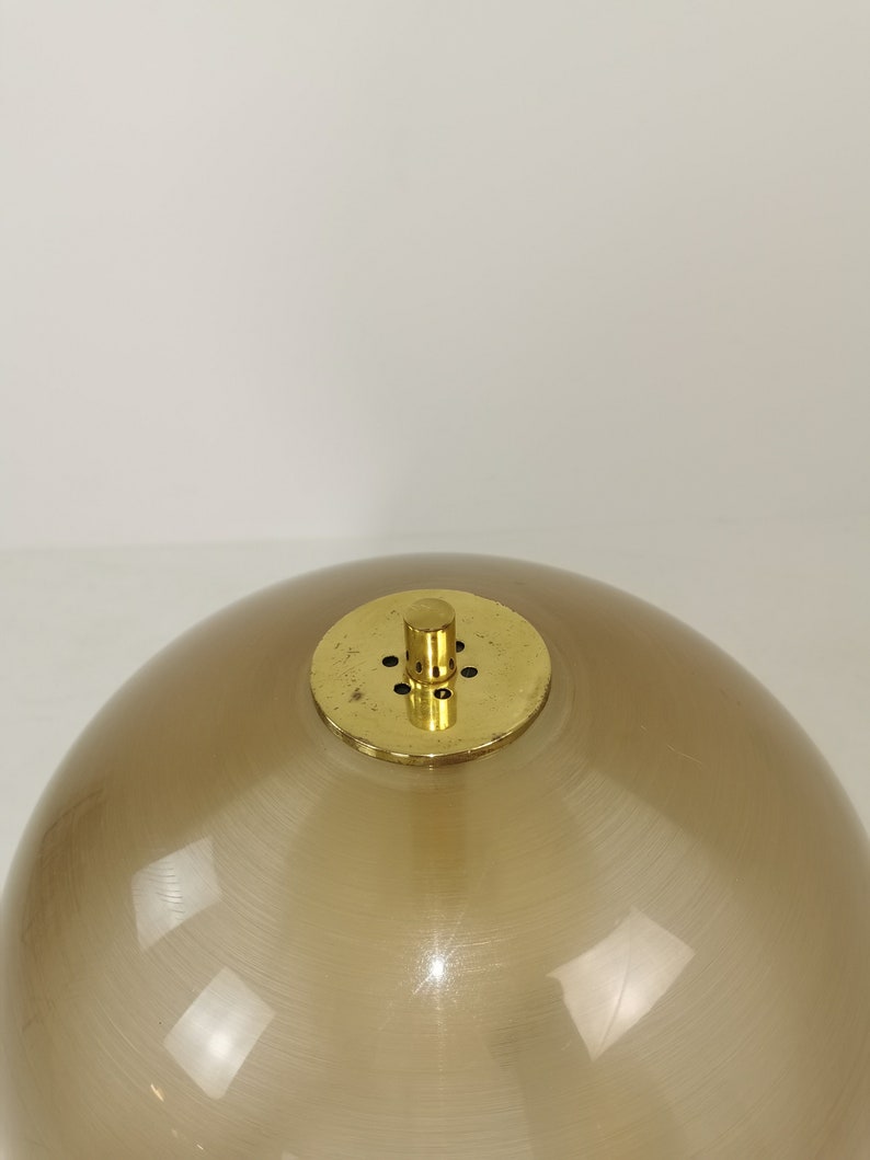 May include: A brown glass globe lampshade with a brass top and a small brass knob. The lampshade has a smooth, shiny finish.