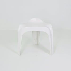 Puede incluir: Un taburete de plástico blanco con un diseño curvo único. El taburete tiene cuatro patas y una columna de soporte central. La forma general es suave y moderna, adecuada para diversos entornos. El taburete está hecho de un material sólido y duradero.