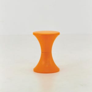 Może przedstawiać: Jaskrawopomarańczowy stołek o gładkiej sylwetce w kształcie klepsydry. Stołek posiada okrągłe siedzisko i pasującą okrągłą podstawę, połączone zwężającą się, wklęsłą częścią środkową, która tworzy jednolitą i spójną formę.