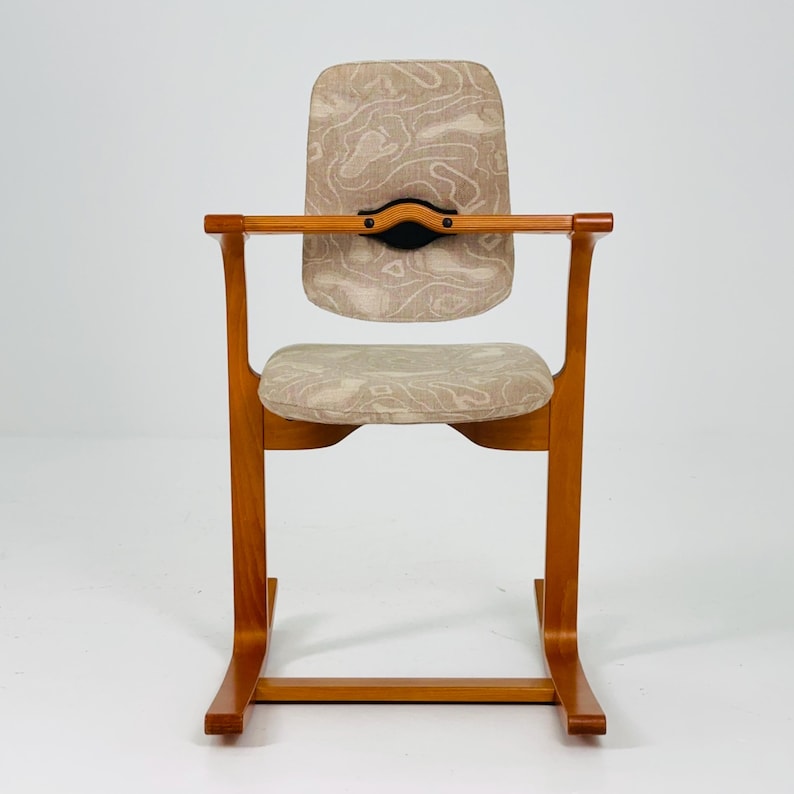 Pode incluir: Uma cadeira de madeira vintage com um design curvo. A cadeira apresenta um tecido estampado castanho claro no assento e no encosto. Os apoios de bra&ccedil;os s&atilde;o horizontais e a cadeira tem uma base curva &uacute;nica. A madeira tem um acabamento quente e natural.